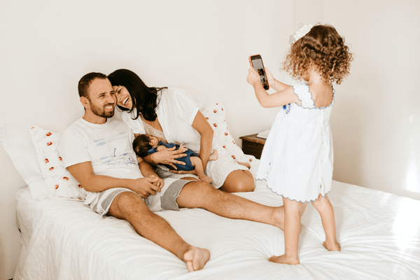 A family laugh in bed as their daughter takes a photo.