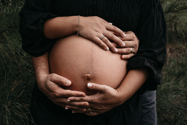 Two sets of hands hold a pregnant belly in a loving embrace